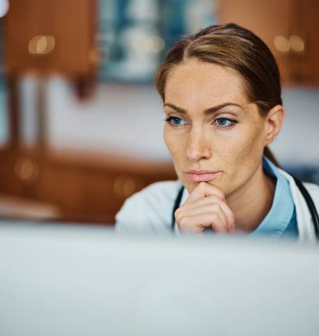 Pensive doctor working on her desktop PC at doctor's office.